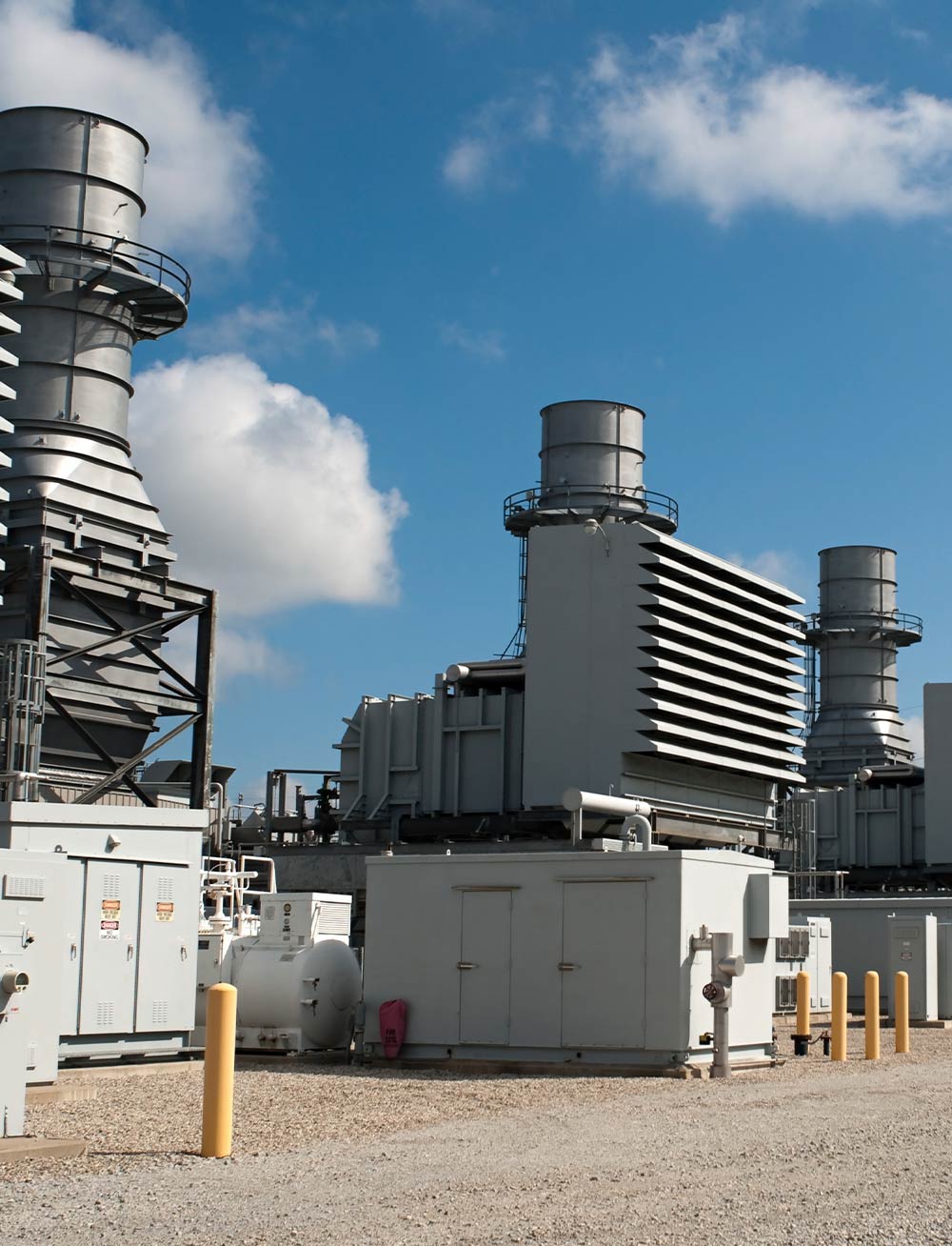 Industrial buildings and machinery with chimneys under a blue sky and scattered clouds.