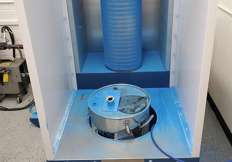 A blue industrial filter machine with a cylindrical filter and a metal container inside a larger enclosure.